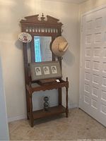 Full view of the coat rack showing wood frame, mirror, upper shelf, and lower shelf with decorative top finial and turned legs.