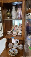 Overview of wooden display cabinet interior showing teacup sets, plates, and glass vases on shelves