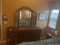 Full view of wooden dresser with ornate carved wood frame and six drawers, with three-panel mirror attached, in a bedroom setting.