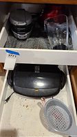 George Foreman electric grill placed inside a drawer with Oster blender jar beside it and a plastic strainer in front.