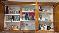 Interior shelves of a wooden cabinet showing assorted glassware, mugs, plastic cups, and some kitchen items.