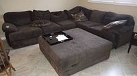 Full view of the large brown sectional couch with matching square ottoman and several pillows arranged on the couch.