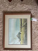 Frontal view of the framed wall art showing a rustic barn in a rural landscape with grass and water, predominantly green and earth tones.