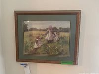 Framed wall art showing a painting of three children in vintage clothing in a grassy field with wildflowers, double matted and wooden frame, measuring about 19x22 inches.