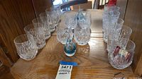 Wide shot of the 8 etched Waterford crystal glasses on wooden surface showing variety of glass shapes and etched designs along with small decorative accents.