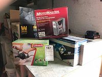 Wide shot showing four boxed air pumps and compressors: two MotoMaster multi-function digital air compressors, one Pit Stop air compressor, and one Coleman quick air pump box.