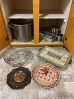 Photo of cupboard contents with large stock pot, metal baking pans, sifters, and glass and ceramic dishes