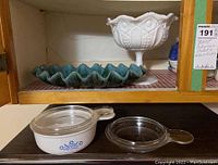 Blue Mountain Pottery dish with greenish turquoise glaze and ruffled edge alongside white milk glass pedestal dish with embossed floral pattern and scalloped rim