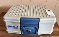 Front view of beige Brinks portable safe showing blue lock mechanism and Brinks Home Security logo.