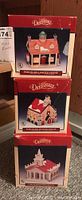 Photo showing three stacked Lemax Dickensvale collectible porcelain lighted houses in original red boxes, each box displaying a different house design.