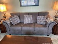 Front view of gray microsuede couch with three patterned throw cushions and lamps on wood side tables