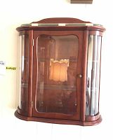 Front view of wood wall-mounted display cabinet showing curved glass door and side panels