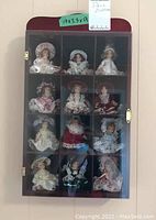 Front view of the dark stained wooden doll display cabinet with clear plastic door and twelve compartments holding porcelain dolls