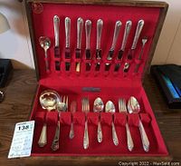 Photo showing the open wooden box containing silverplate flatware items arranged in red felt lining with loops holding each piece.