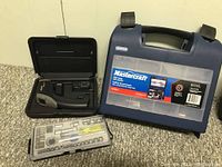 Raytek laser thermometer tester inside black case, next to Mastercraft drill case and socket organizer tray on carpeted floor.