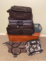 Stacked Heys nesting suitcases (3 sizes), folding shoe storage bag, cooler bag in packaging, and plastic basket shown on wooden chest