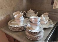 Stacked dinner plates, bread and butter plates, cups, saucers, teapot, creamer, and sugar bowl on a kitchen counter.