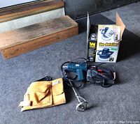 Photo shows the Skil jigsaw, yellow leather tool belt, black heat tool, and boxed 10-inch orbital car waxer arranged on a carpeted floor.