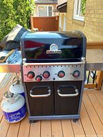 Front view of Broil King Baron grill with closed lid, stainless steel control panel and two propane tanks on deck