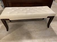 Front view of the white leather tufted bench with dark wood legs