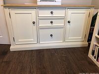 Front view of white cabinet showing three drawers and two cupboard doors