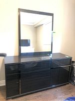 Front view of the black wood dresser with attached matching mirror showing drawers and doors.