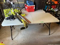 White plastic folding table with black metal legs, shown from a side angle to give clear view of size and condition.