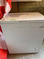 Front view of white chest freezer with closed lid in garage, Canadian flag behind