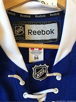 Close-up view of the neckline of the blue Leafs NHL Reebok authentic jersey showing Reebok label, NHL logo patch, size 54 tag, made in Canada label.