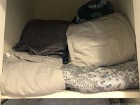 Shelf with folded sheets and comforters in beige, gray and patterned fabrics