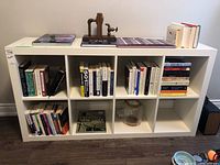 Front view of the white shelving unit showing books inside and decorative items on top and in shelves.
