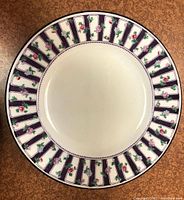 Single porcelain luncheon plate with detailed decorative border of purple stripes and small pink and red flowers with green leaves on white background.