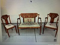 Full view of 3-piece parlor set including one settee and two chairs, showing needlepoint floral upholstery and marquetry with mother of pearl inlay on wood frames.
