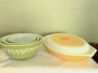 Four Pyrex pieces on a white surface: three green 'Crazy Daisy' mixing bowls nested and one yellow 'Sunflower' oval casserole with lid.