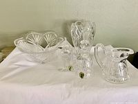 Five pieces of Waterford cut crystal displayed on white cloth, showing bowl, vase, pitcher, bell, and paperweight. All pieces clear and cut with intricate patterns.