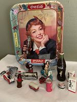 Full lot view including vintage Coke tray and twelve Coca-Cola advertising collectibles of various types, sizes, and colors.