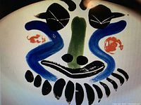 Close-up of the painted abstract face design in black, blue, green, and red brush strokes.