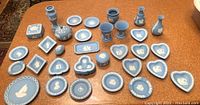 Full view of 38 pieces of Wedgwood jasperware in light blue with various shapes including heart-shaped, round, tri-lobed, small vases, covered boxes, and dishes featuring white relief decoration