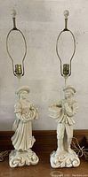 Pair of Chapman mid-century figural lamps, male and female figures, cream ceramic, standing on ornate bases, photographed against a wall