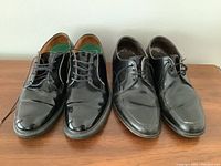 Two pairs of men's black leather derby dress shoes side by side showing polish and soles.