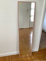 Front view of the full length mirror leaning against a wall, showing rectangular shape and pink frame.