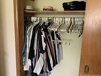 Closet rail with multiple XL men's shirts, sweaters, suits, and trousers hanging on hangers along with some folded clothes on top shelf.