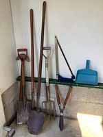 Photo showing full view of big lot of gardening tools including various shovels, hedge shears, fork, saw and dustpan