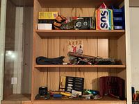 Woodworking accessories on wooden shelves including cleaning materials, cables, electrical tape, and wood spade bits in packaging.