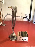 Full view of Holcomatic Mark XII floor buffer with coiled power cord next to a box of assorted pads and brushes on a red floor.