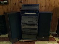 Full system setup with all components stacked in an audio rack cabinet flanked by two large speakers. The rack has a glass door that is closed.