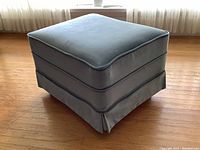 Blue velvet-textured corduroy ottoman shown from a front angle, highlighting pleated skirt and piping details