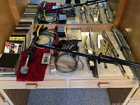 Wide view showing multiple musical accessories laid out on a wooden surface. Includes music stands in folded and partially assembled positions, cables, microphone, tuner, and media.