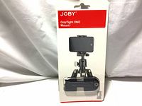 Photo of the front of the sealed retail packaging showing the Joby GripTight ONE Mount with an attached smartphone mounted on a small tripod.