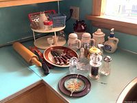 Overall view of vintage kitchenware arranged on a corner counter with a wooden rolling pin, plate with knives, ceramic shakers, and glass swan sculpture